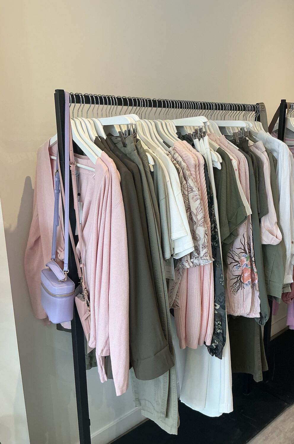 A black rail of pink knits, olive green pieces and white tops with a lilac bag hanging from the end